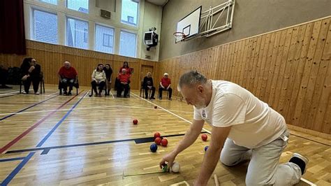 Hráči boccie v akcii, s asistentmi a rampami na špeciálne upravenom ihrisku.
