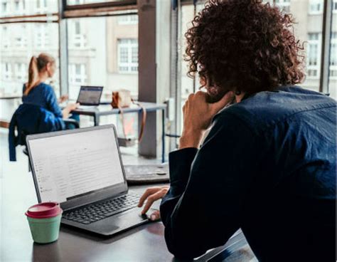 Osoba držiaca šálku kávy s otvoreným notebookom, pozerajúca na text